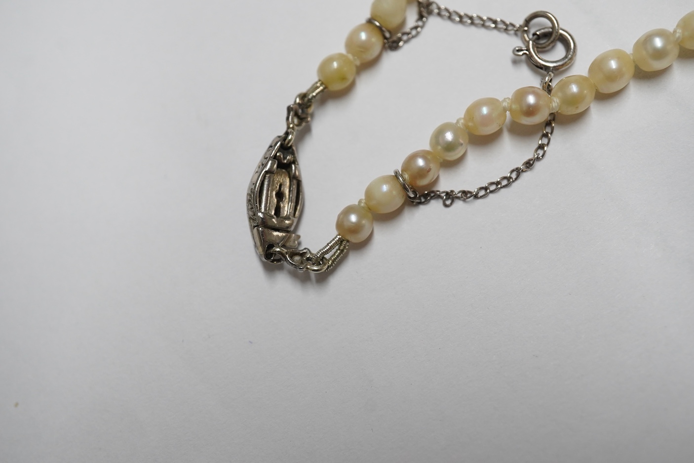 A single strand graduated cultured pearl choker necklace, with a three stone diamond set engraved white metal clasp, 36cm